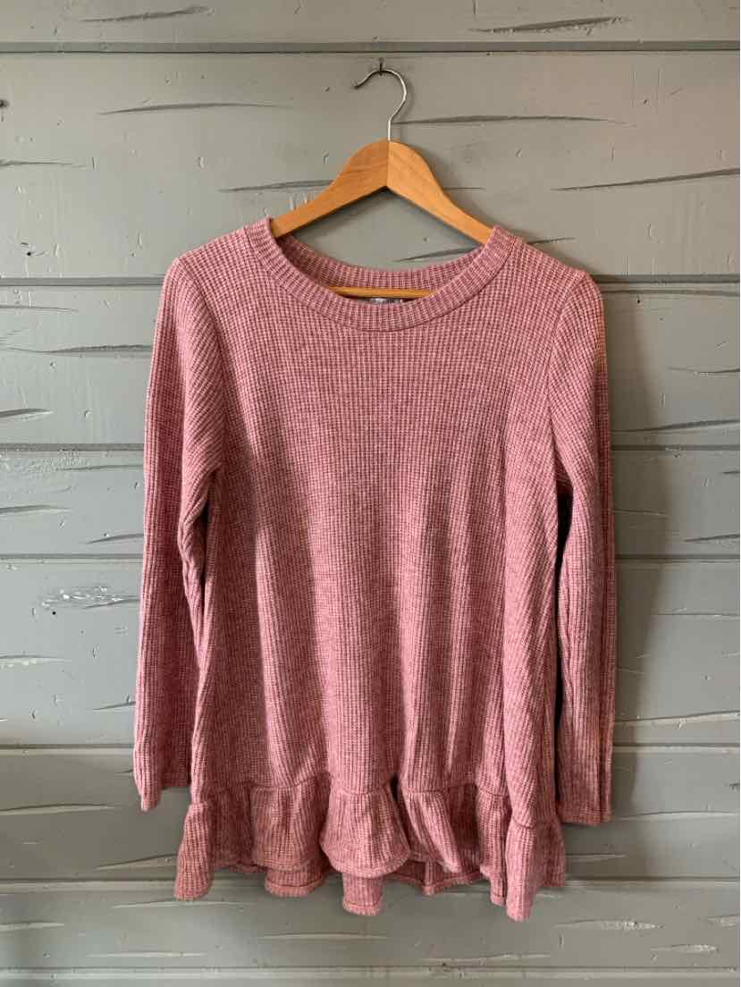 Pink long-sleeve waffle knit top with round neckline and ruffled hem hanging on wooden hanger.