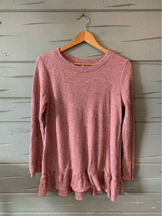 Pink long-sleeve waffle knit top with round neckline and ruffled hem hanging on wooden hanger.