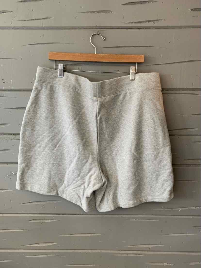 Light gray high-waist shorts with elastic waistband and loose fit hanging on wooden hanger against gray wall.