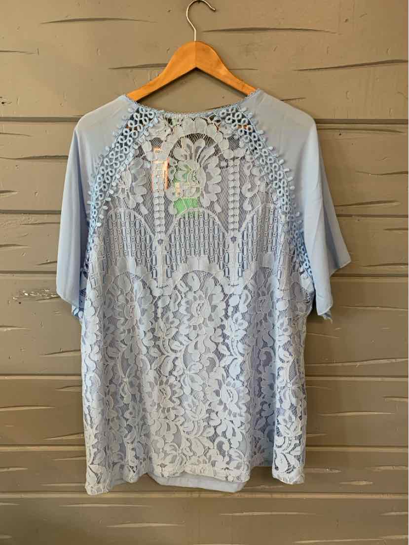 Light blue short-sleeve blouse with floral lace back and solid fabric front, relaxed fit, size 2XL.