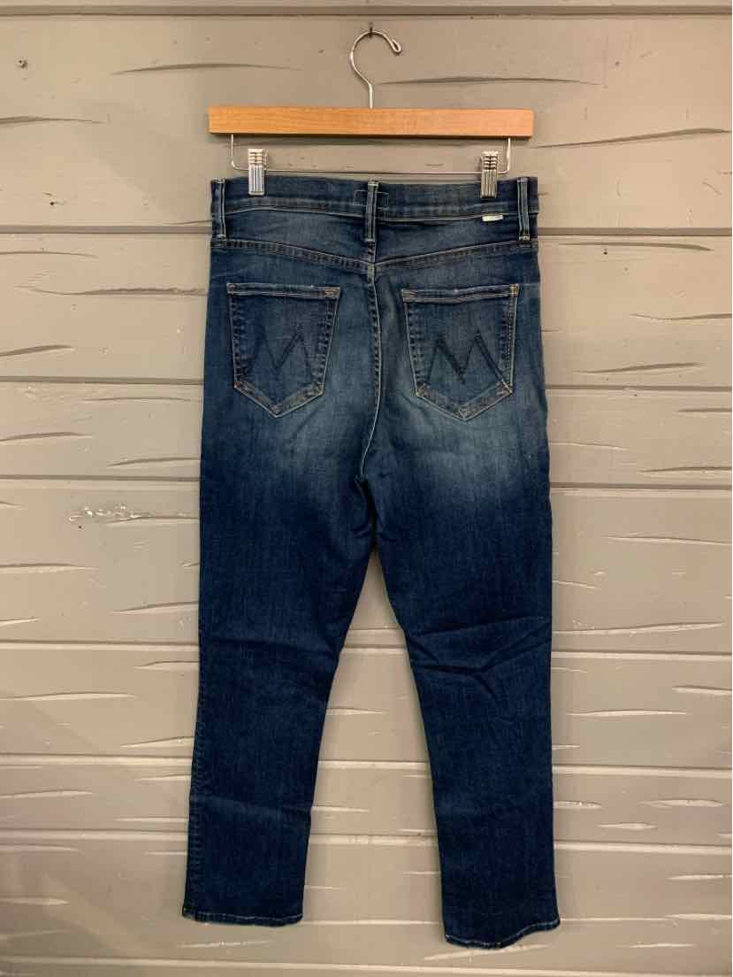 Dark blue denim jeans with faded detailing and stitched back pockets hanging on wooden hanger against light wooden wall.