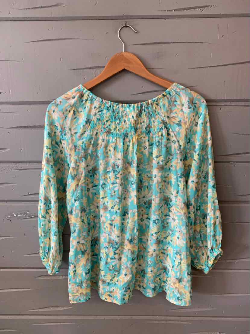 Teal floral blouse with loose fit and three-quarter sleeves hanging on wooden hanger.