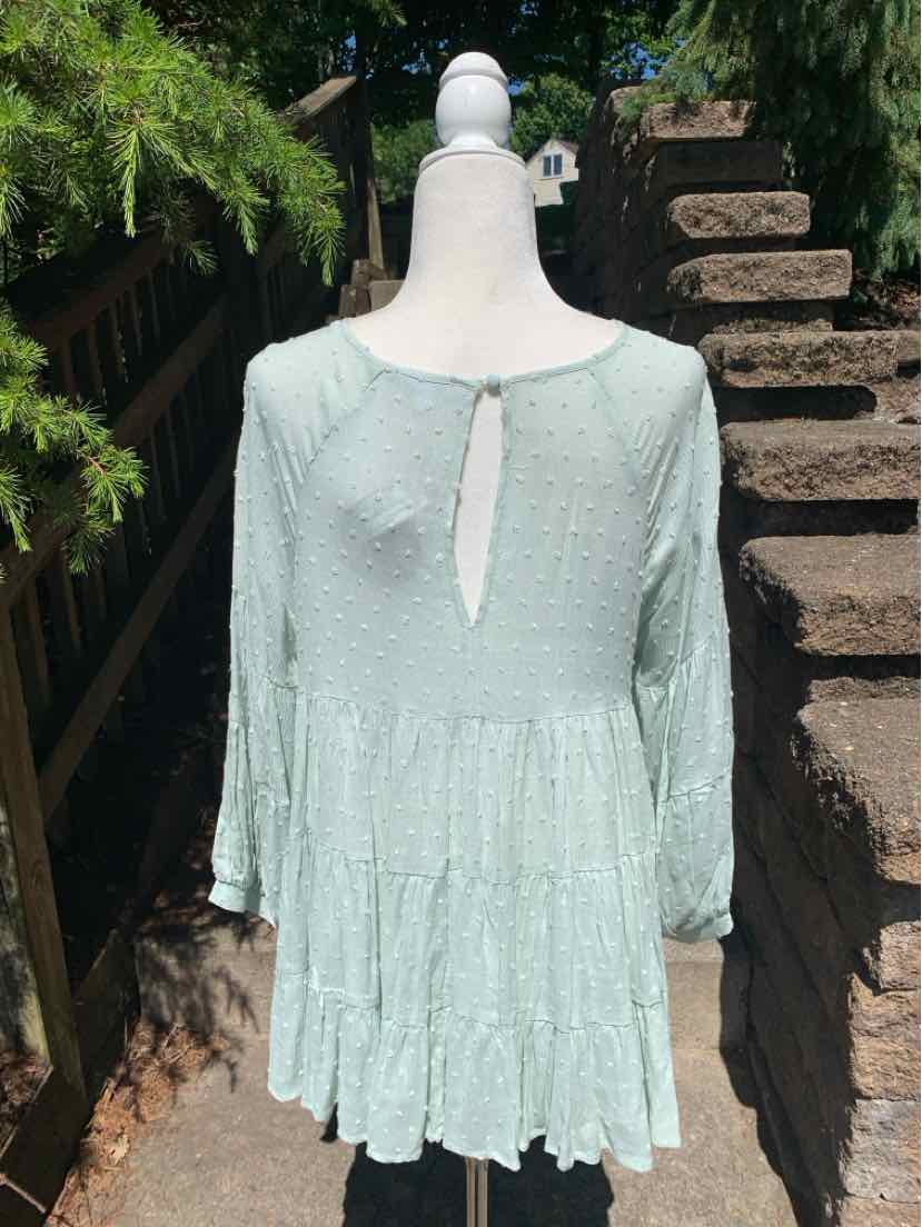 Light green loose-fit blouse with three-quarter sleeves and ruffled tiers, keyhole back with button closure.