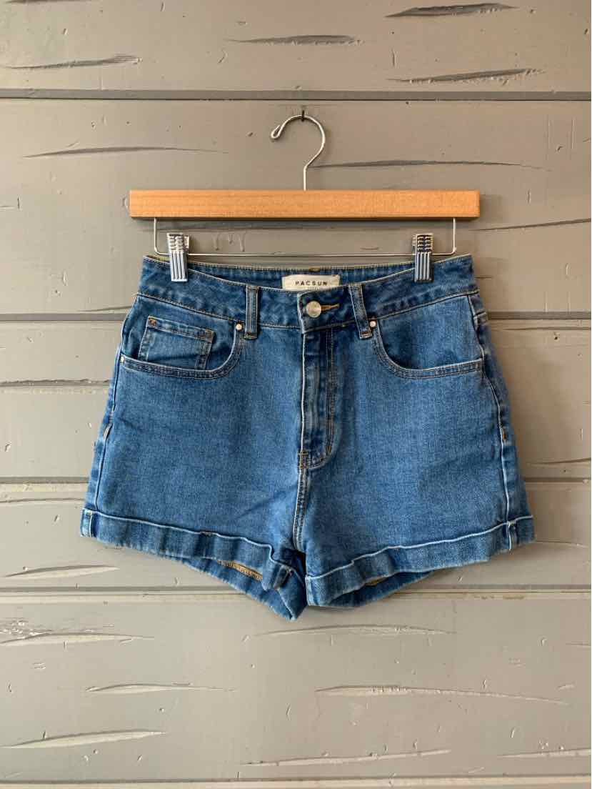 Blue denim women's shorts with front pockets and button closure hanging on wooden hanger.