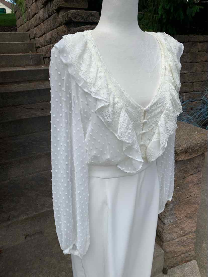 White long-sleeve lace blouse with ruffled V-neck and textured dotted fabric.