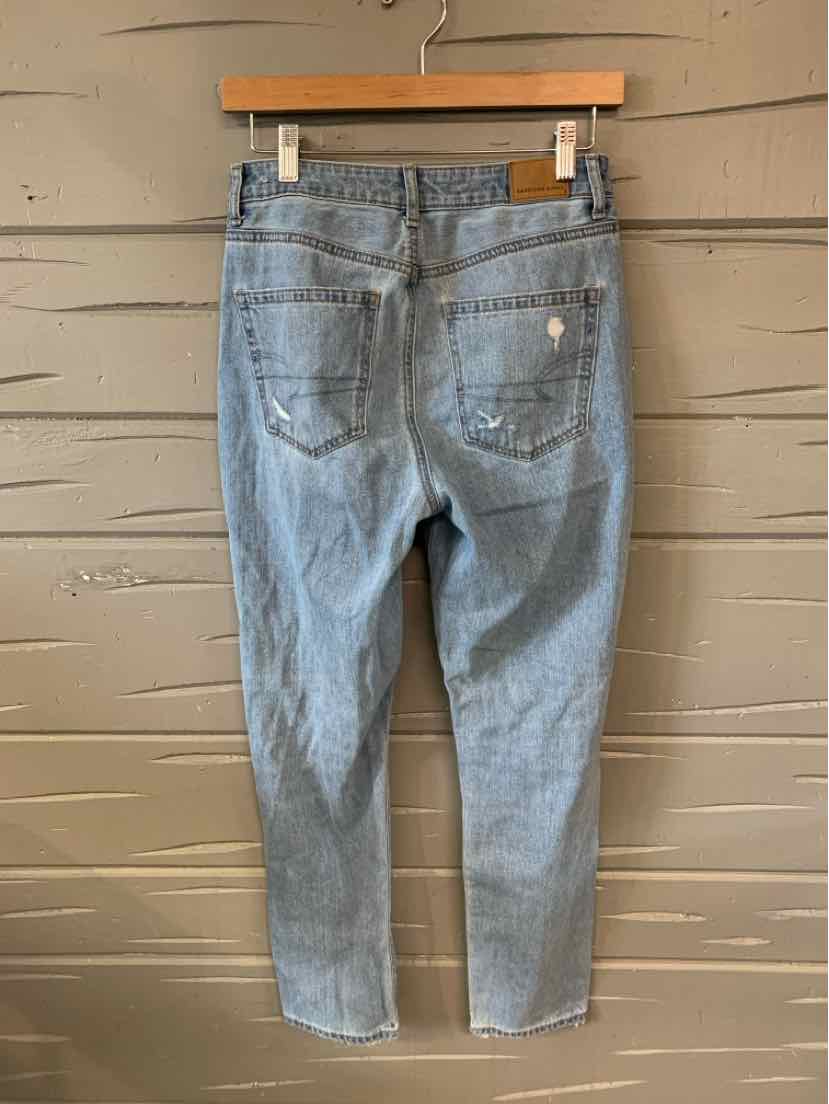 Light blue denim jeans with high waist and slightly tapered legs, featuring two back pockets and subtle distressing on right .