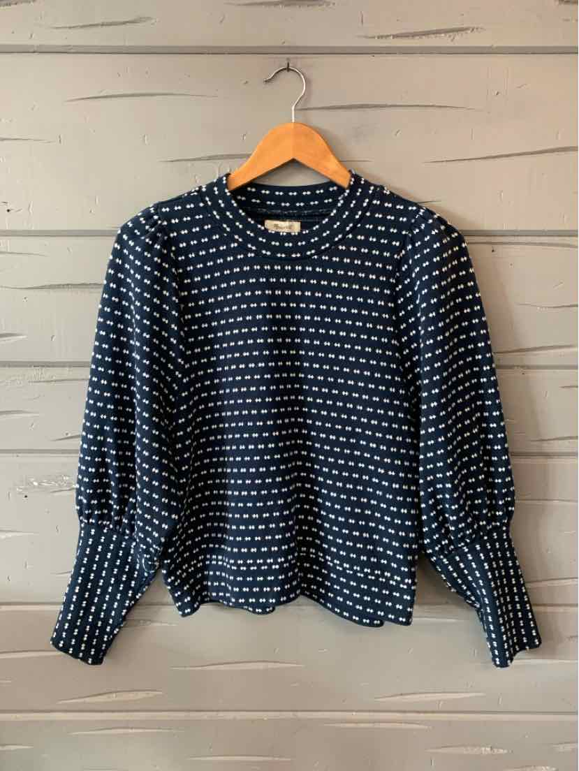 Navy blue long-sleeve sweater with white diamond pattern and ribbed cuffs hanging on wooden hanger.