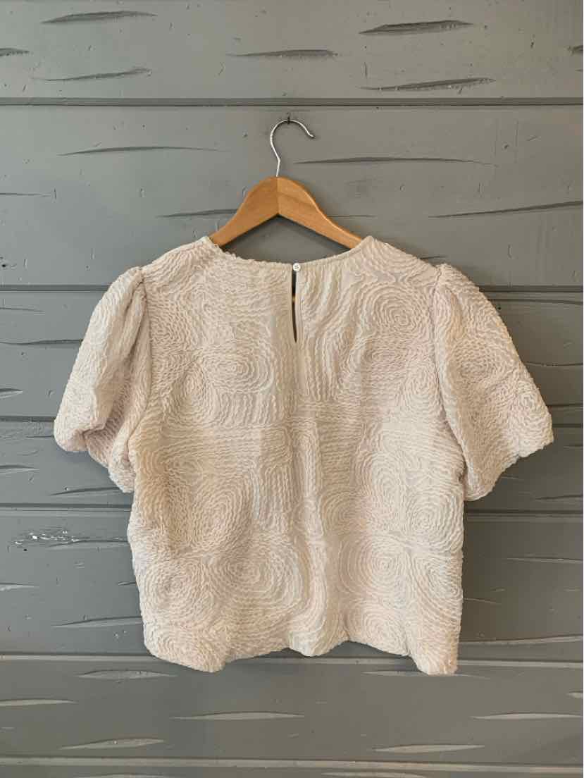 Beige textured short-sleeve blouse with subtle puff shoulders and rounded neckline on wooden hanger.