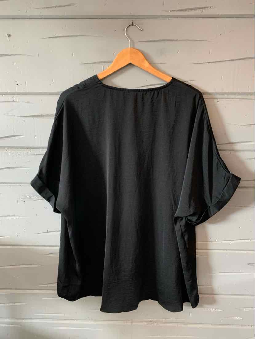 Black oversized short-sleeve top with rolled cuffs and a relaxed fit on wooden hanger.