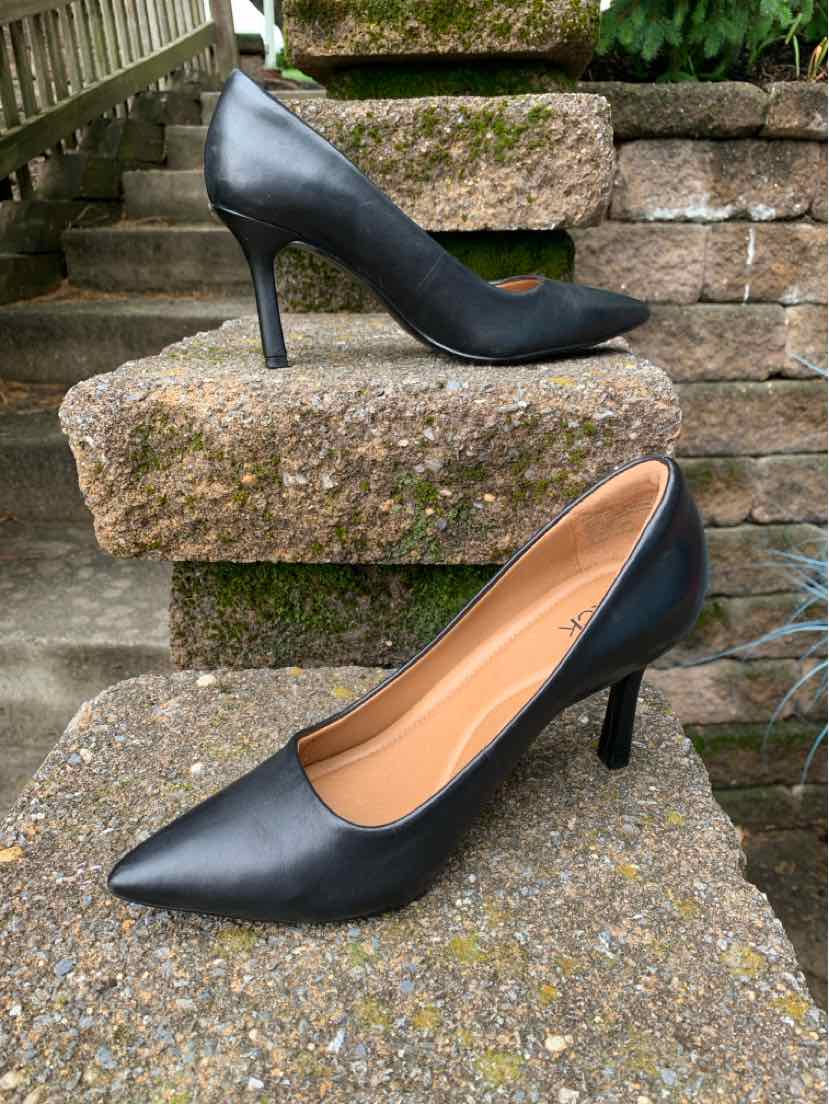 Black pointed-toe leather high heels with kitten heel on outdoor stone steps.