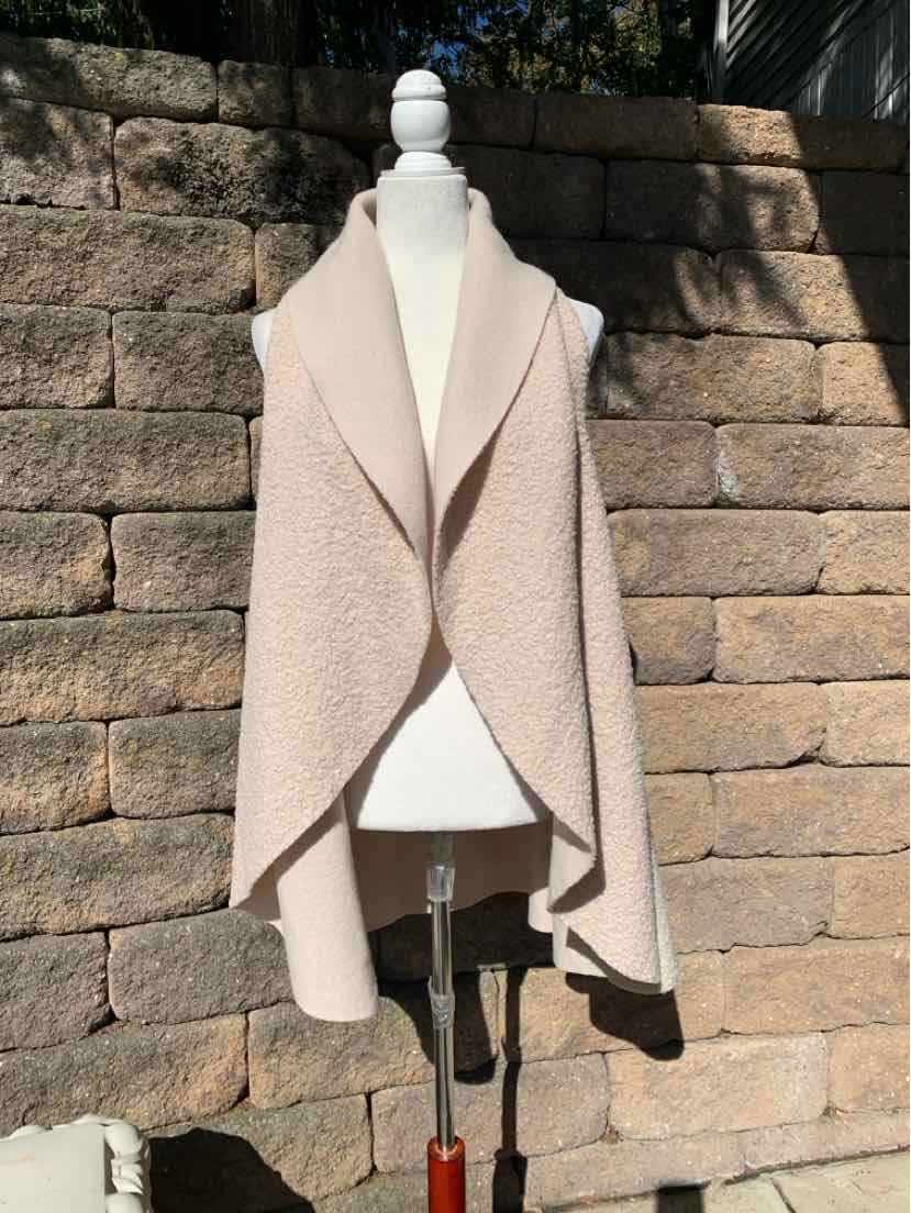 Beige bouclé open-front coat with wide shawl lapels, draped panels, and long sleeves.