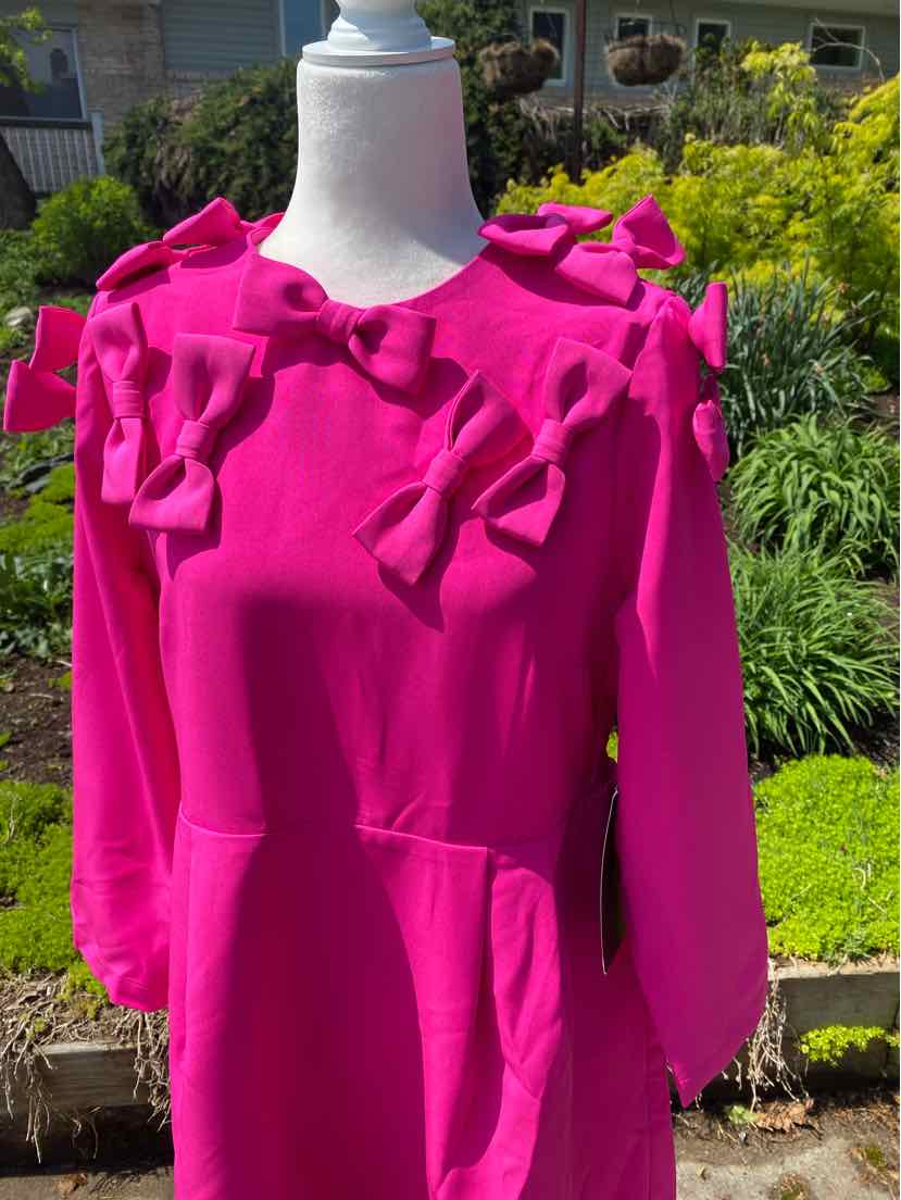 Bright pink long-sleeve top with large fabric bows on shoulders and chest.