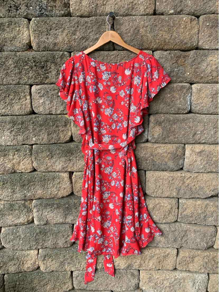 Red floral wrap dress with flutter sleeves and side tie belt hanging on wooden hanger.