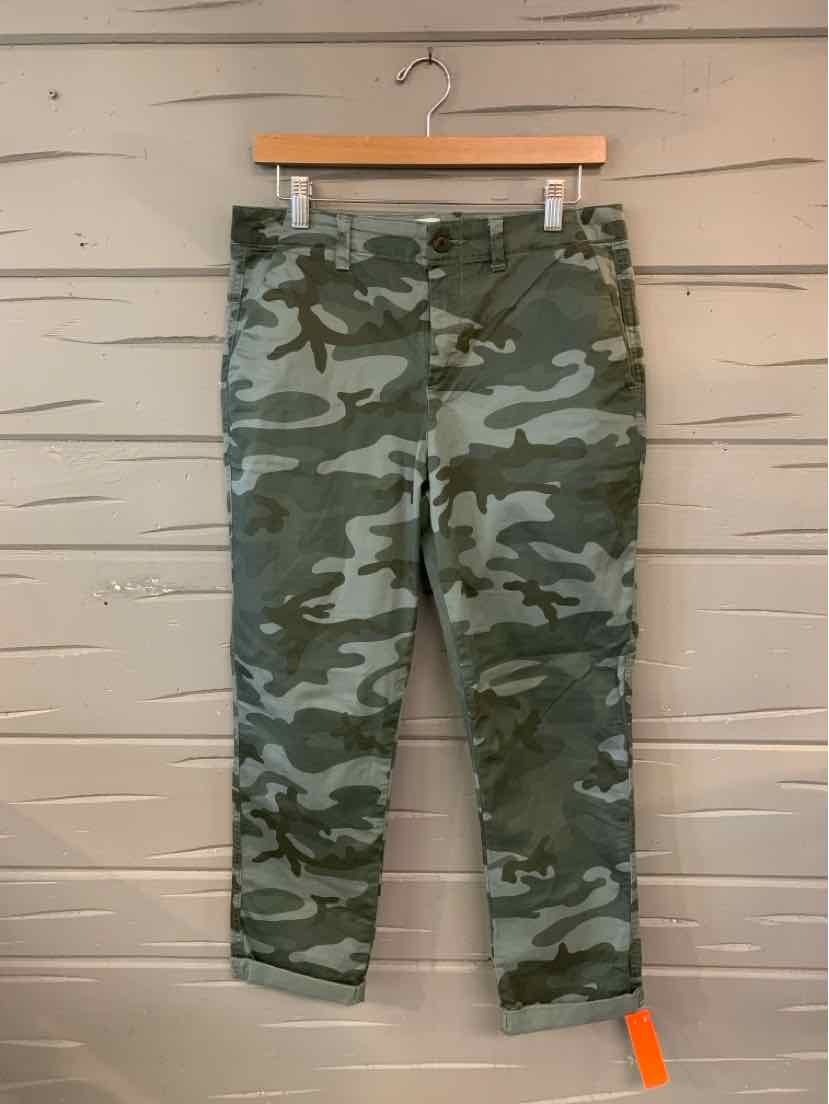 Green and gray camo ankle-length pants with cuffed hems hanging on a wooden hanger.