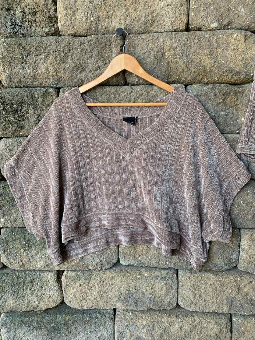 Brown chenille knit cropped sweater with wide V-neck and loose short sleeves on wooden hanger against stone wall.