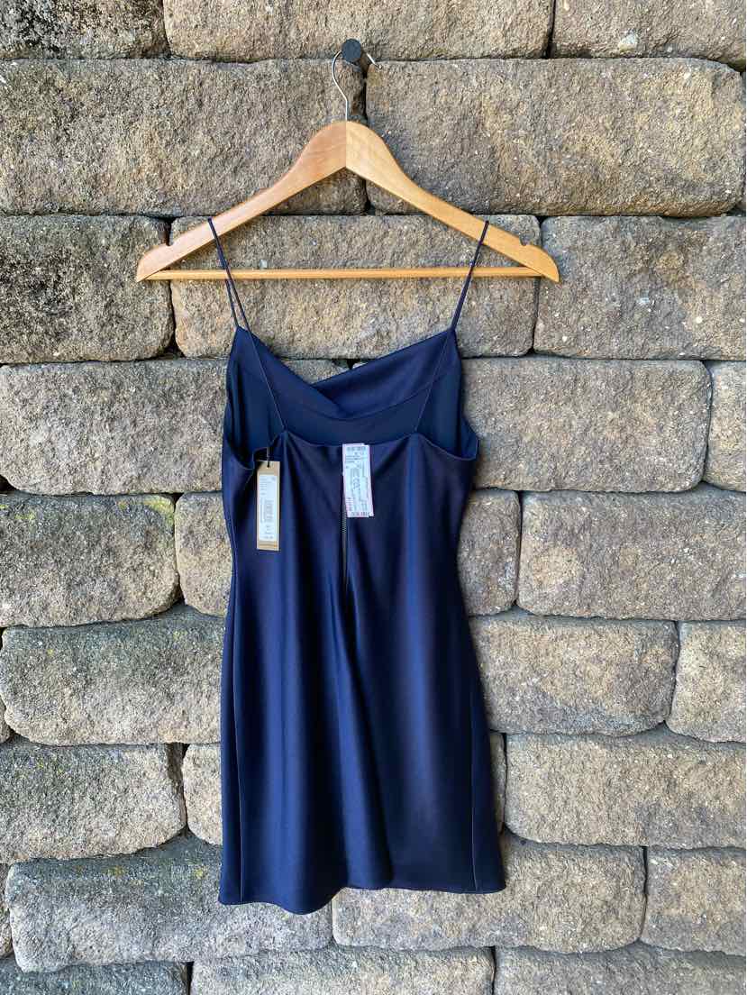 Navy blue satin strapless dress with draped bodice and slight sheen hanging on wooden hanger against stone wall.