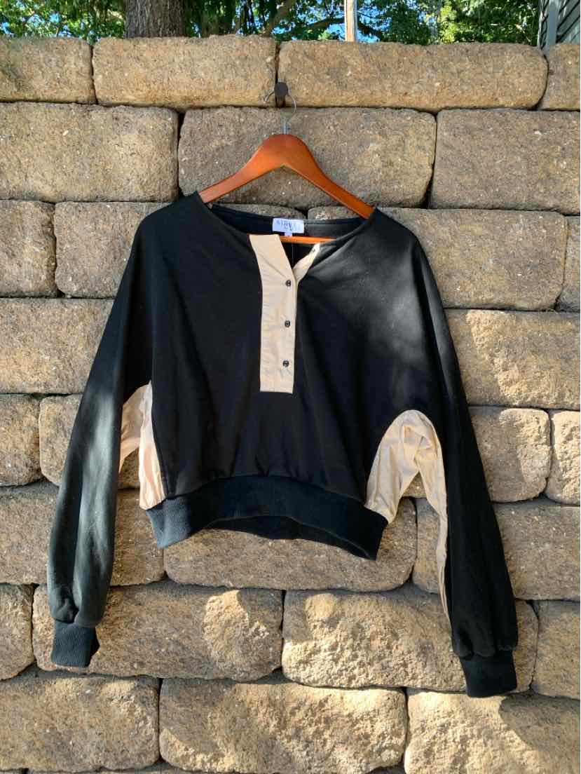 Black long-sleeve pullover with beige buttoned placket and beige inner sleeve detail, relaxed fit.
