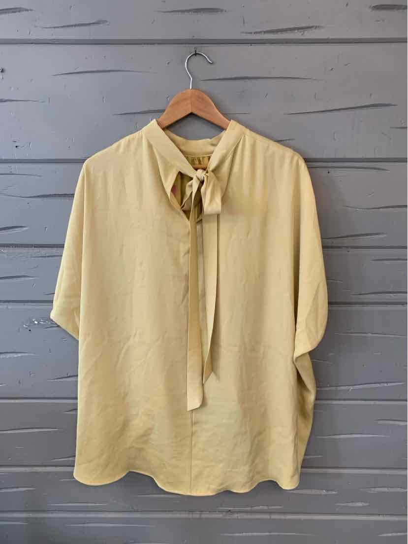 Light yellow blouse with a tie-neck and loose fit, hanging on wooden hanger.