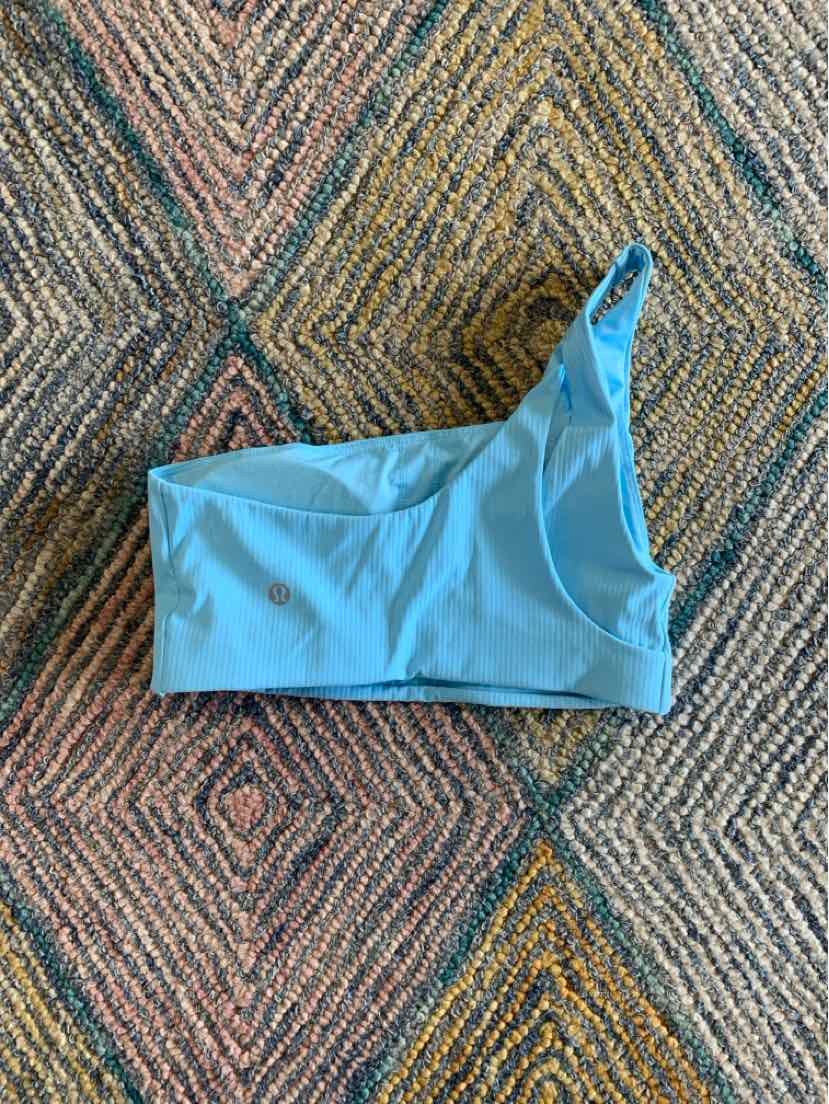 Light blue, seamless athletic sports bra with one wide strap and scoop neckline on patterned fabric background.