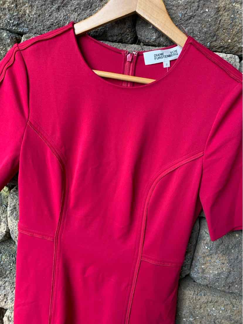 Bright pink short-sleeve dress with seam detailing and round neckline on wooden hanger.