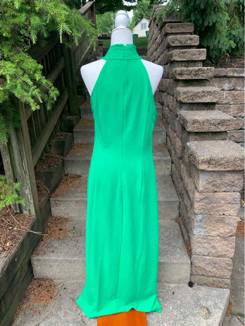 Green sleeveless halter-neck maxi dress with flowing skirt on white mannequin outdoors.