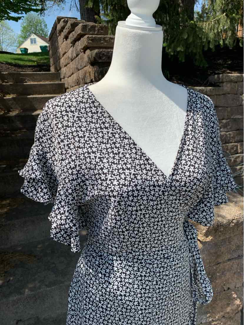 Black floral wrap dress with short puff sleeves and V-neck on mannequin outdoors.
