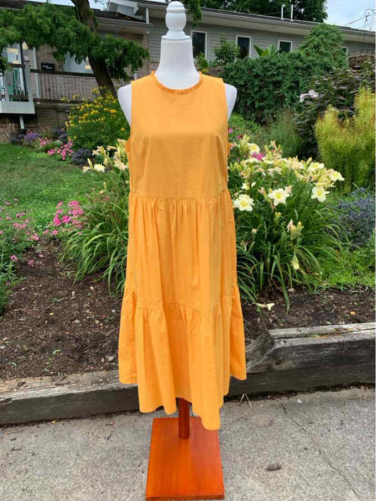 Sleeveless orange midi dress with tiered skirt and round neckline on mannequin outdoors.