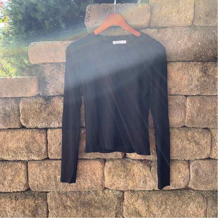 Black long-sleeve fitted crew neck top made from smooth fabric hanging on wooden hanger against stone wall background.