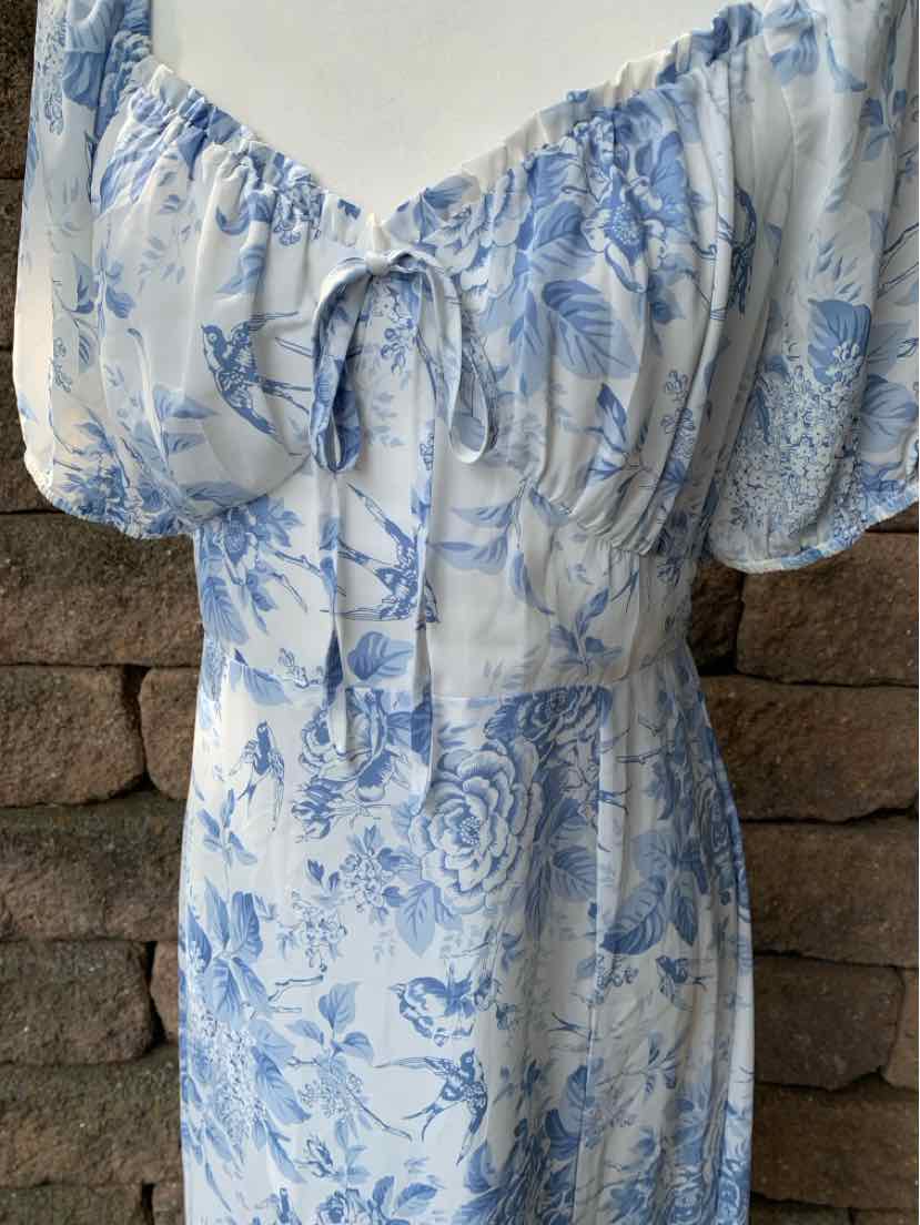 White dress with blue floral pattern, puffed short sleeves, and gathered neckline with tie detail.