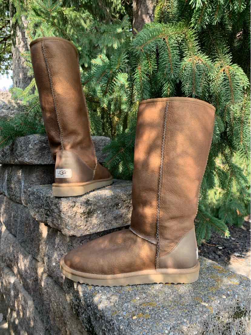 Pair of tall brown suede UGG boots with rounded toes, cuffed shafts, and thick tan soles.