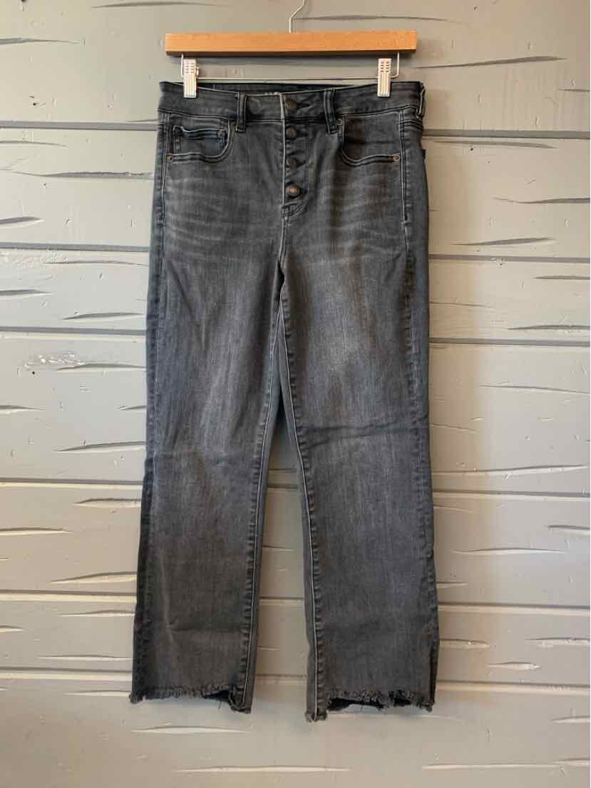 Gray denim jeans with raw hem and straight leg cut hanging on wooden hanger.