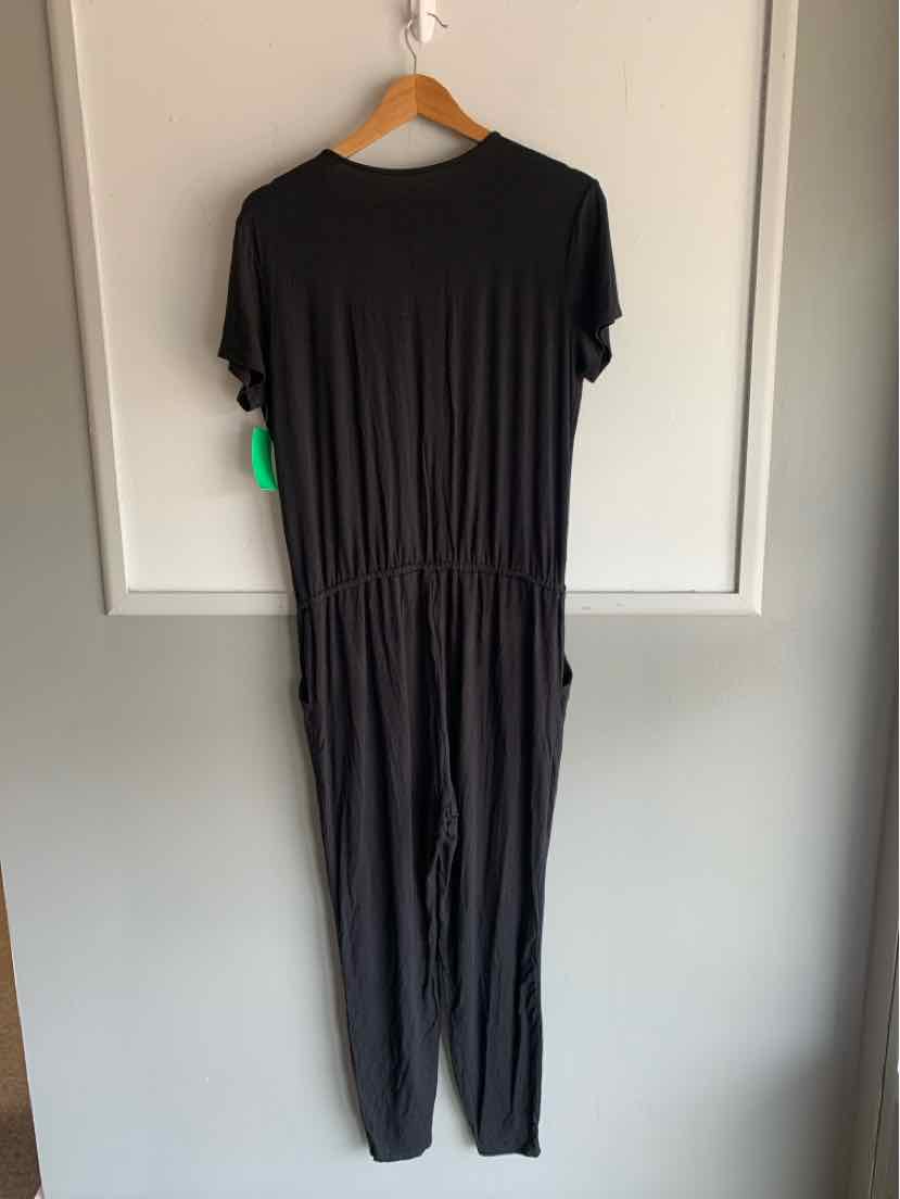 Black short-sleeve jumpsuit with gathered waist hanging on wooden hanger against white door.