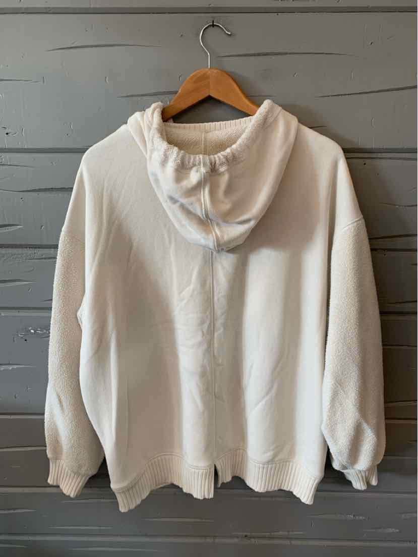 Cream-colored hoodie with long sleeves and a relaxed fit hanging on wooden hanger.