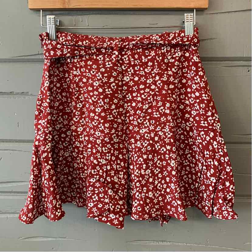 Red floral mini skirt with ruffled hem and elastic waistband hanging on wooden hanger.