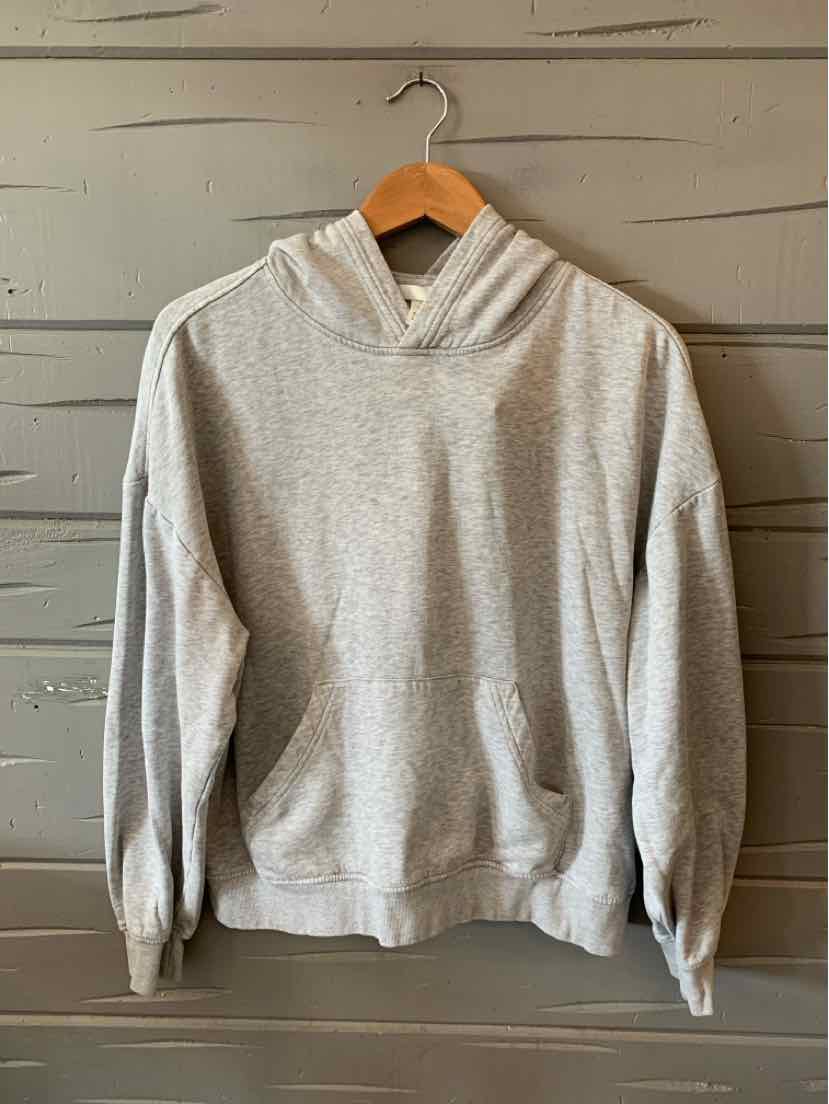 Light gray cotton hoodie with kangaroo pocket and ribbed cuffs hanging on wooden hanger.