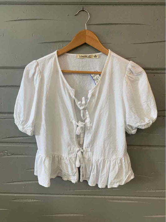 White short puff sleeve blouse with ruffle hem and front tie details on wooden hanger.