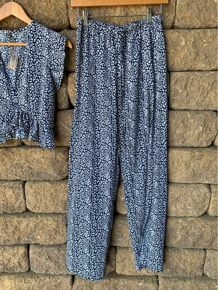 Blue floral print pants with elastic waistband and tapered legs hanging on wooden hanger.