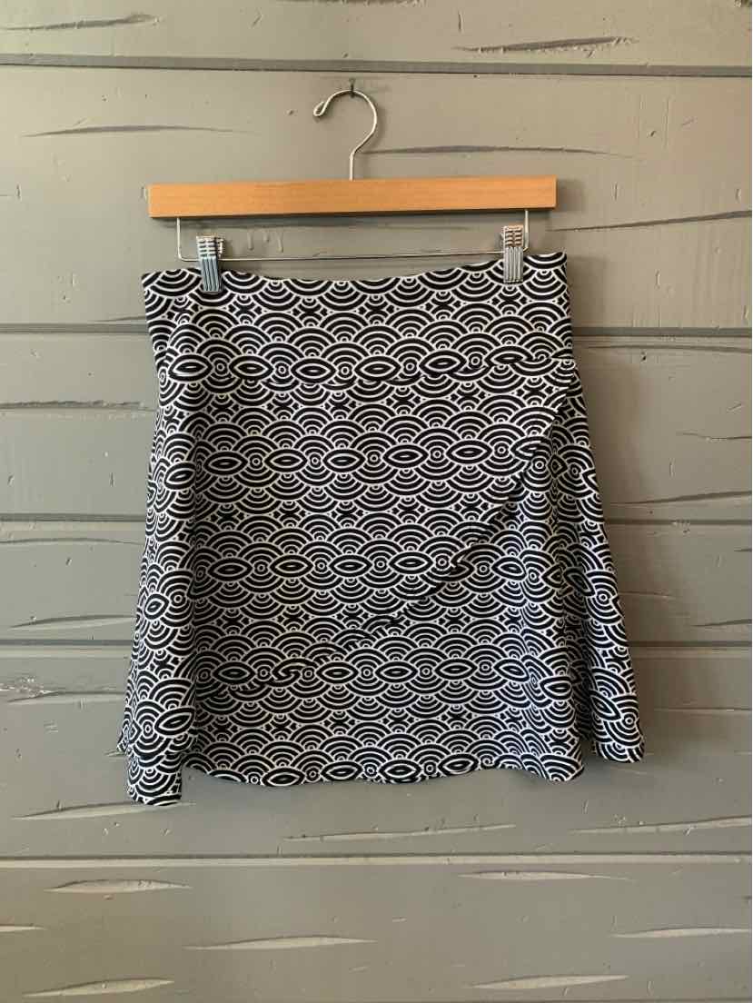 Black and white geometric patterned mini skirt with asymmetrical front overlay on wooden hanger.