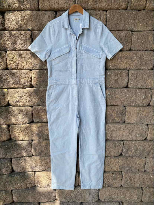 Light blue short-sleeve jumpsuit with front pockets and a collar, hanging on a wooden hanger.