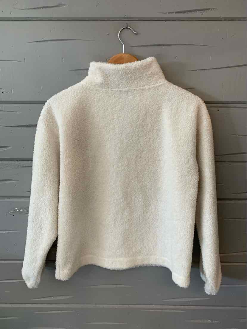 Off-white sherpa fleece pullover with high neck and relaxed fit hanging on wooden hanger.