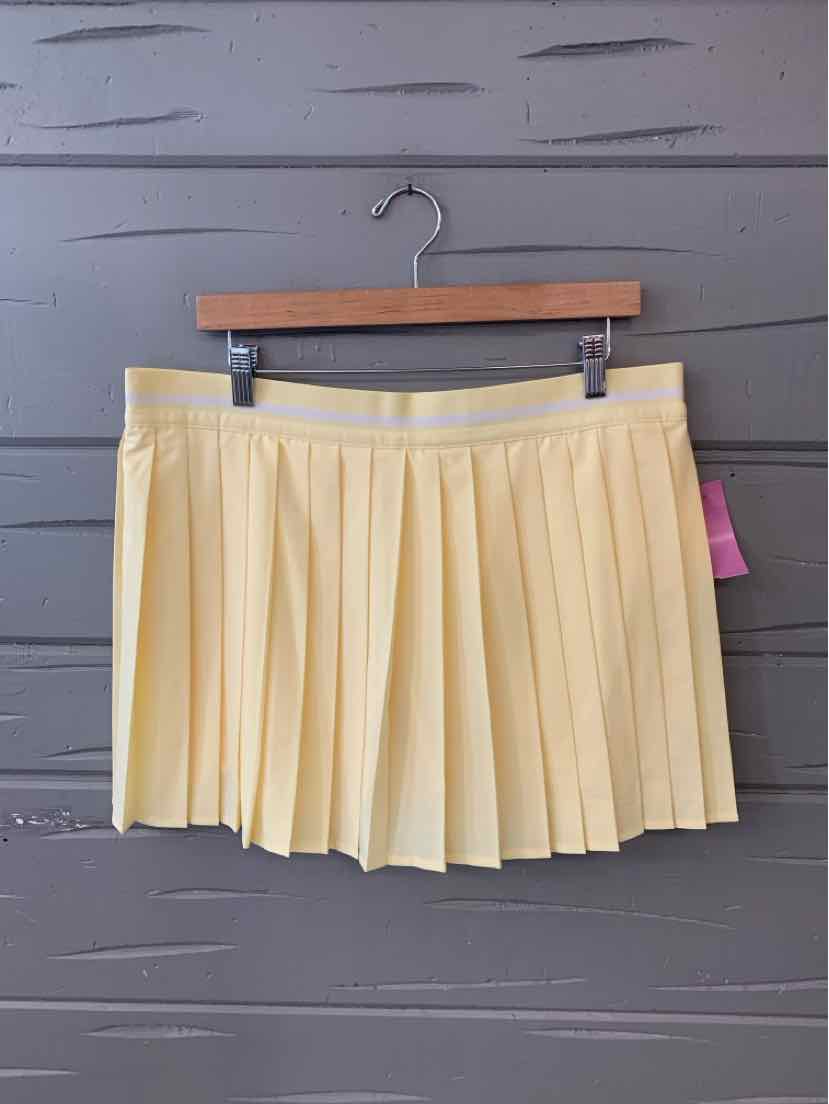 Yellow pleated skort with waistband hanging on wooden hanger against gray wood wall.