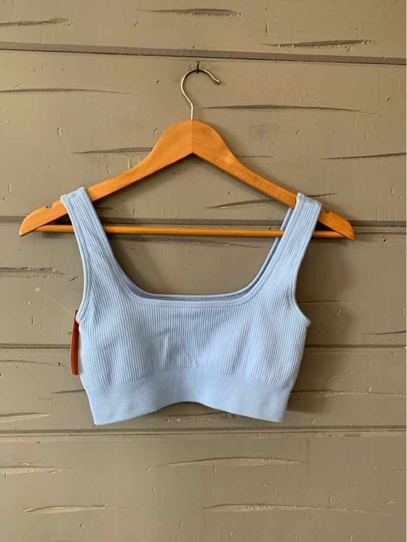 Light blue cropped tank top with wide shoulder straps on wooden hanger against beige wall.