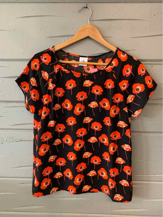 Black short-sleeve blouse with bright orange floral print and round neckline on wooden hanger.