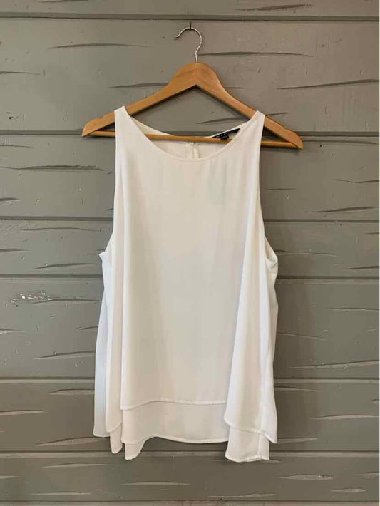 White sleeveless flowy blouse with boat neckline, layered hem, hanging on wooden hanger.