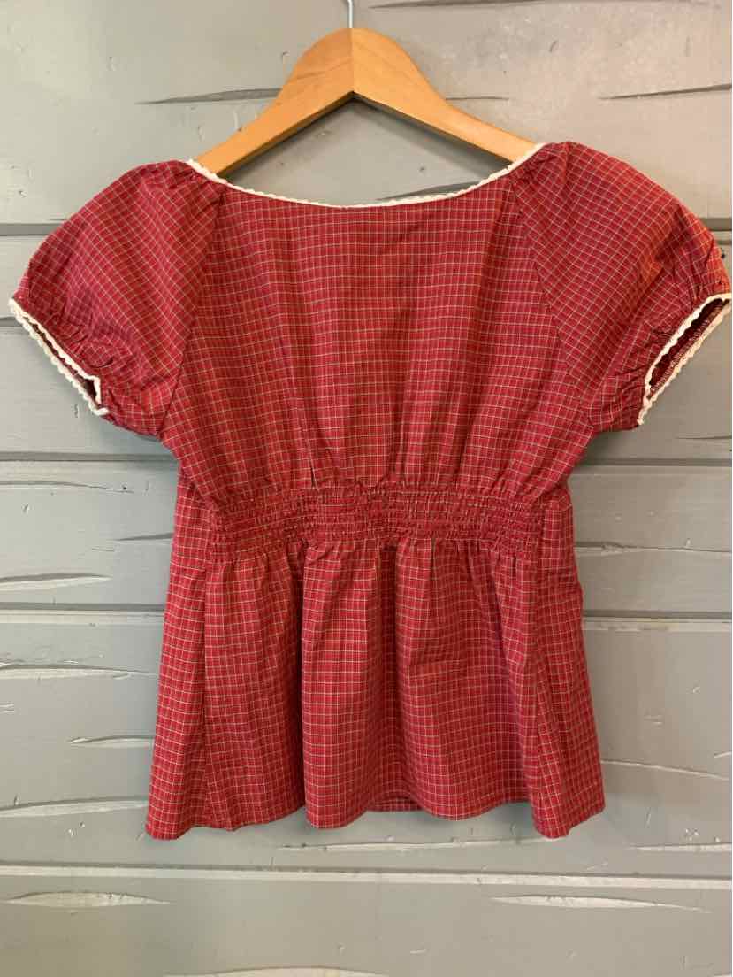 Red plaid short-sleeve blouse with gathered waist and white-trimmed cuffs hanging on wooden hanger.