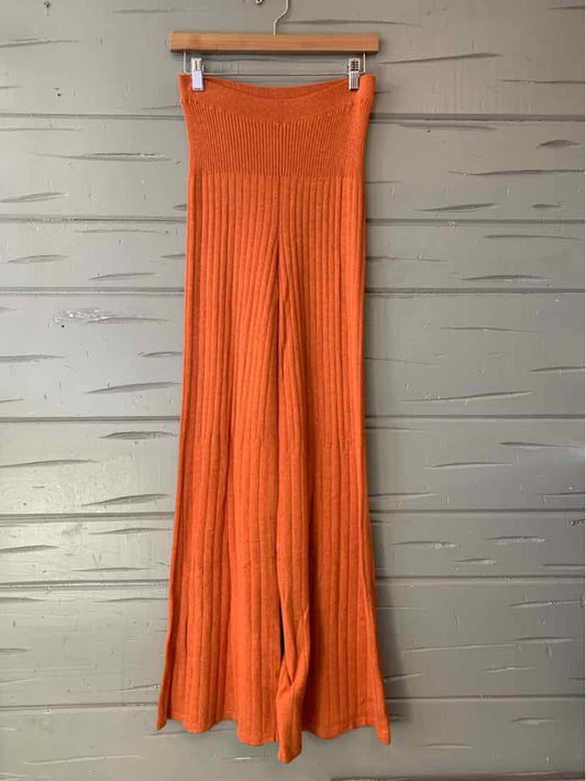 Orange wide-leg knit pants with high ribbed waistband hanging on wooden hanger.