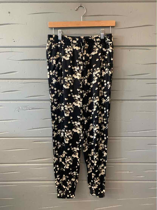 Black tapered pants with white and beige floral print, elastic waistband, and cuffed ankles, size XS.