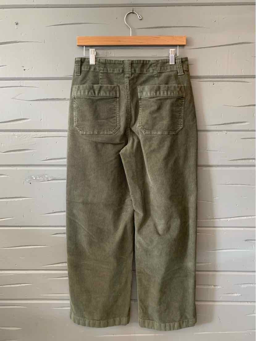 Olive green corduroy pants with wide legs and two back patch pockets hanging on wooden hanger.