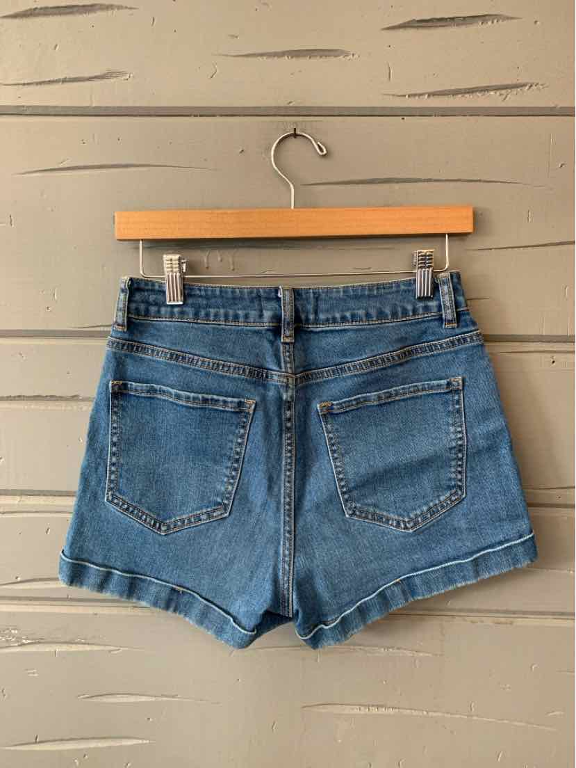 Blue denim high-waist shorts with back pockets and a slightly frayed hem hanging on a wooden hanger.