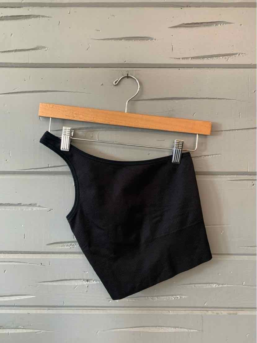Black one-shoulder cropped athletic top with smooth fabric on wooden hanger against gray wooden background.